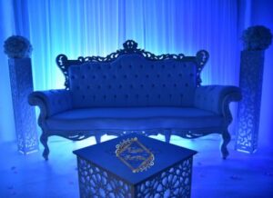 Somptueux canapé baroque blanc, éclairage bleu intense. Décoration de mariage avec colonnes fleuries et table basse gravée portant le logo "Events For You".