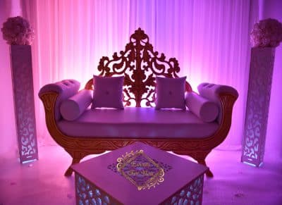 Somptueuse décoration événementielle: canapé royal, piédestaux fleuris et éclairage lounge violet. Table avec le logo "Events For You".