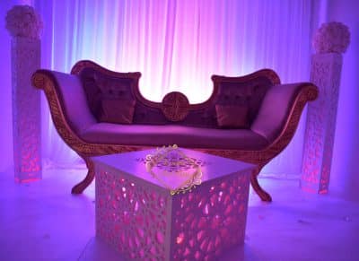 Canapé de réception violet capitonné et table basse ajourée éclairée par des lumières d’ambiance pour un événement de luxe.