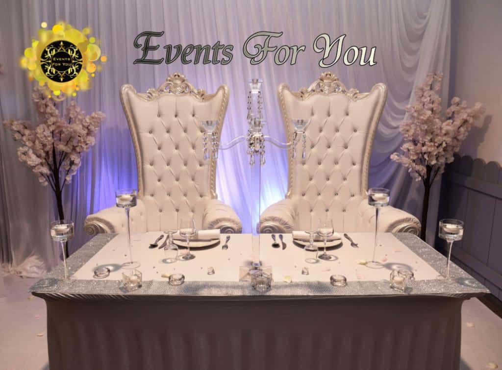 Table d'honneur Events For You avec deux chaises trônes blanches capitonnées, bougeoirs, et décorations florales de cerisier sur fond violet.