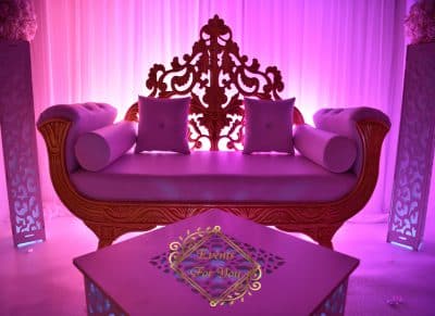 Trône de mariage baroque or et mauve sous éclairage magenta intense. Décoration événementielle luxueuse. Table gravée avec "Events For You".