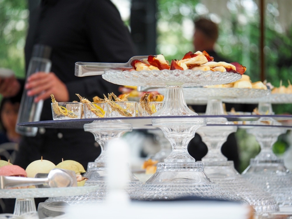 Buffet de mariage somptueux sous les lumières Vaste buffet de réception en extérieur : tartes salées, salades, mignardises et assiettes empilées, éclairé par des guirlandes chaudes.